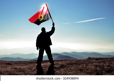 Successful Silhouette Man Winner Waving Angola Flag On Top Of The Mountain Peak