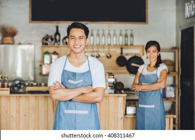 Successful Small Business Owner Standing With Crossed Arms With Partner At The Background