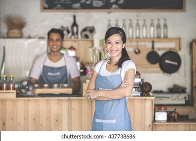 Successful Small Business Owner Standing With Crossed Arms With Partner At The Background