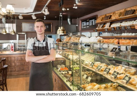 Successful small business owner standing behind the counter and smiles with employee in bakery background