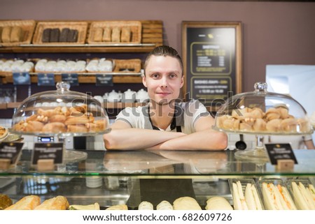 Successful small business owner standing behind the counter and smiles with employee in bakery background