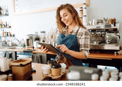 Successful small business owner stands behind the counter of coffee shop with digital tablet, takes order. Portrait of beautiful woman barista. Business concept of seller-entrepreneur - Powered by Shutterstock