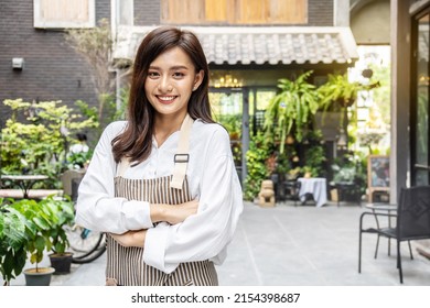 Successful small business young asian owner woman standing with looking at camera posing crossing arms, Portrait of waiter salesman worker wearing apron standing at work space smiling friendly