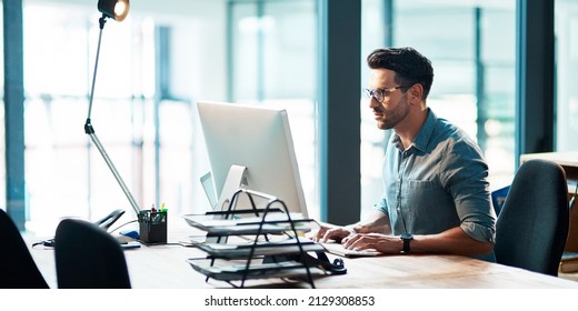 The successful stay consistent. Shot of a focused young businessman using a computer at his desk in a modern office. - Powered by Shutterstock