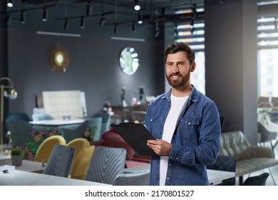 Successful store owner in denim shirt making notes, while working in modern furniture shop. Portrait of handsome designer with tablet smiling at camera, while standing in expo center. Concept of work. - Shutterstock ID 2170801527