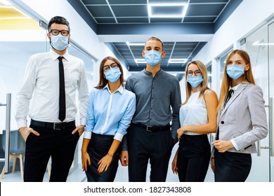 Successful team of business workers, wearing medical protective masks on their face, posing together in a modern office, happy motivated employees demonstrating unity and success