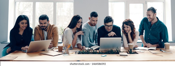 Successful Team. Group Of Young Modern People In Smart Casual Wear Using Modern Technologies While Working In The Creative Office