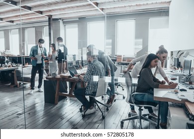 Successful team at work. Group of young business people working and communicating together in creative office - Shutterstock ID 572805178