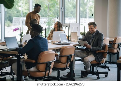 Successful Team Working In Open Plan Business Space Office.
Group Of Happy Multi-ethnic Businesspeople On Casual Meeting At Their Company Board Room, They Talking And Using Digital Tablet And Laptops.