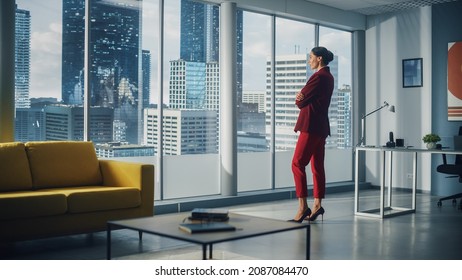 Successful Thoughtful Caucasian Businesswoman Wearing Perfect Red Suit Standing In Office Looking Out Of Window On Big City. Confident Female Corporate CEO Managing Company Investment Strategy