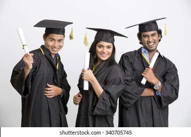 Successful three college graduates wearing cap and gown holding diploma on white background