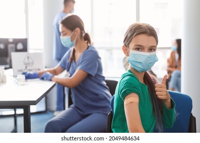 Successful Vaccination. Portrait Of Smiling Young Teen Girl Showing Thumb Up And Vaccinated Arm With Medical Adhesive Bandage Strip After Covid Vaccine Injection. Corona Virus Immunization Campaign