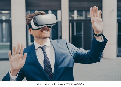 Successful Video Game Publisher Wearing Black And White VR Headset, Amazed Bearded Businessman Trying Out New Immersive Virtual Reality Game, Playing Outside, Building In Blurred Background