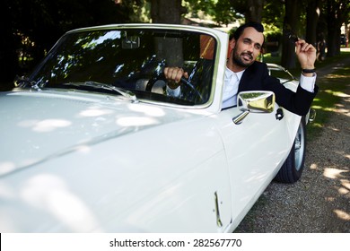 Successful And Wealthy Businessman Sitting Behind The Wheel Of His Luxury Cabriolet Car On Countryside Road, Sure And Confident Handsome Man Sits In His New Convertible Car Outdoors Looking So Happy