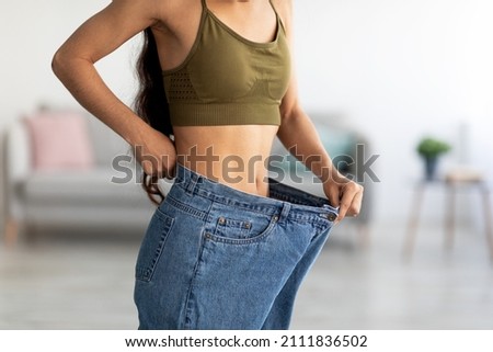 Successful weight loss diet concept. Cropped view of young Indian lady in big jeans demonstrating results of her slimming program, promoting healthy eating at home, closeup