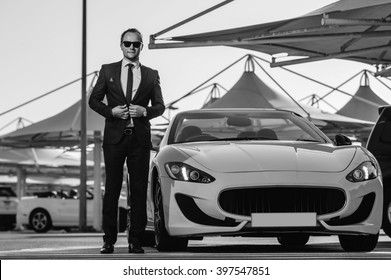 Successful yang businessman stands next to yellow cabrio car.