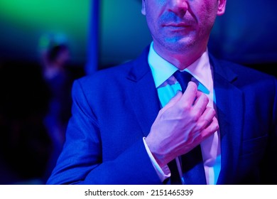 Successful Yet Seedy. Shot Of A Seedy Businessman Adjusting His Tie In A Go Go Bar With A Woman Dancing On A Pole Behind Him.