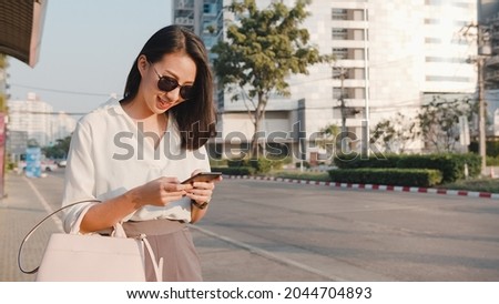 Successful young Asia businesswoman in fashion office clothes hailing on road catching taxi and holding smart phone while standing outdoors in urban modern city. Business on the go concept.