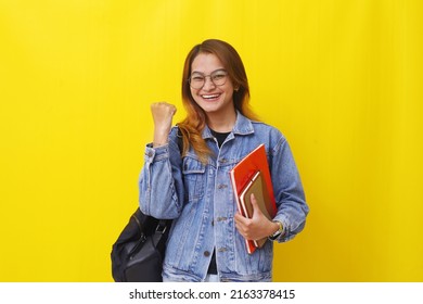 Successful Young asian college student standing while holding books and clenching hand.