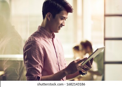 successful young asian entrepreneur looking at tablet computer in office