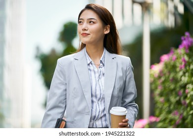 successful young asian female white collar office worker walking on street looking away holding cup of coffee
