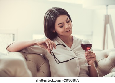 Successful Young Beautiful Woman Sitting On A Sofa In The Living Room. Drinking Red Wine.