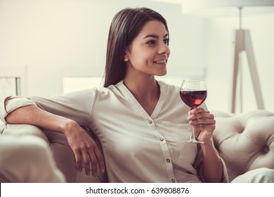 Successful Young Beautiful Woman Sitting On A Sofa In The Living Room. Drinking Red Wine.