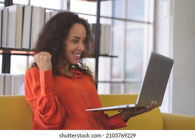 Successful Young Black Woman Wearing Orange Shirt Exciting And Using Laptop For Video Call On Sofa At Home. Business Woman And Freelance Work From Home In Spreading Of Coronavirus Covid-19.