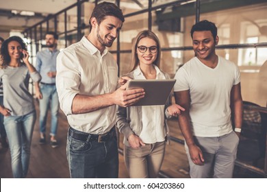 Successful young business people are talking, using a digital tablet and smiling while walking down the corridor in business center - Powered by Shutterstock