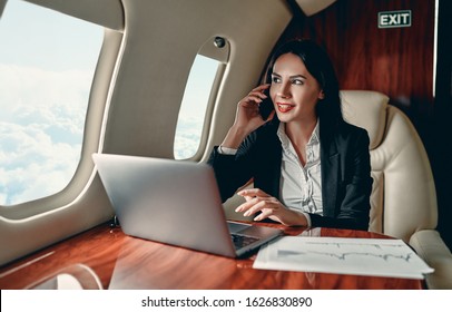 Successful young business woman working with laptop and speaking on mobile phone while flying in private jet. - Powered by Shutterstock