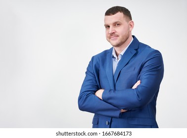 Successful Young Businessman With Crossed Arms Wearing Blue Suit With A Lovely Genuine Smile Posing Against Grey Background With Copy Space