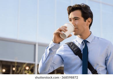 Successful young businessman outside office. Businessman drinking coffee and thinking about his future. Happy ambitious man drinking an hot coffee with a paper cup in front of the modern building.
