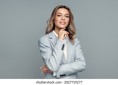 Successful young businesswoman touches chin with her hand, smiling, looking at camera posing isolated on gray background. Studio portrait of confident friendly female lawyer in blazer and blouse