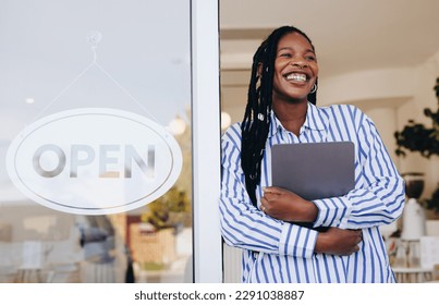 Successful young cafe owner standing next to an open sign at the entrance of her new restaurant. Female small business owner smiling happily while holding a digital tablet in her coffee shop. - Powered by Shutterstock