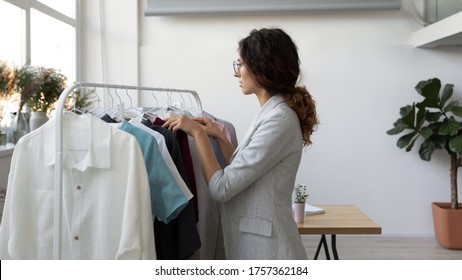 Successful Young Caucasian Female Fashion Designer Or Stylist Manage New Clothes Collection On Rack In Studio Showroom, Millennial Woman Tailor Dressmaker Prepare Wardrobe Clothing For Sale