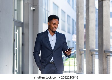 Successful Young Confident African American Businessman Moving With Cellphone In Hands Against Modern Office Building Background Downtown Black Business Man Walks Using A Mobile Phone In Formal Suit