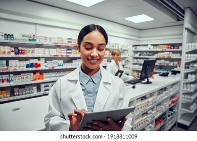 Successful young female pharmacist using digital tablet in drugstore with colleague using computer in background