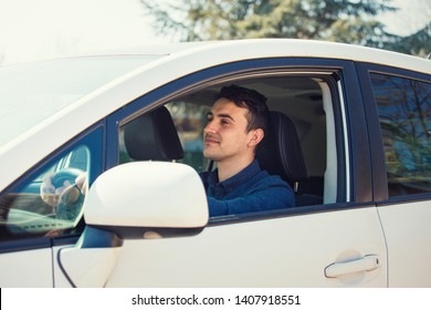 Successful Young Man Driving His New White Car Keeps Hand On The Steering Wheel Looking Ahead Happy Feeling Safe. Confident Businessman Smiling, Enjoying The Ride, Traveling Road Trip Concept.