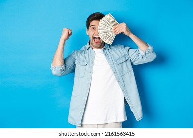 Successful Young Man Earn Money, Making Fist Pump And Showing Cash, Winning Prize Or Receive Credit, Standing Over Blue Background