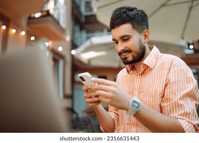 Successful young man student freelancer using laptop, watching webinars, working remotely, e-learning e-commerce online in street cafe.