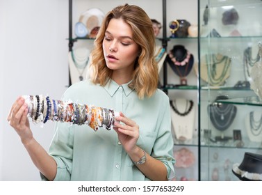 Successful young saleswoman demonstrating colorful bracelets from different precious stones in jewelry shop - Shutterstock ID 1577653249