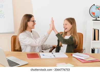 Successful young tutor teacher mother babysitter nanny helping her daughter student schoolgirl with homework, test, exam, new topic giving high five at home school.