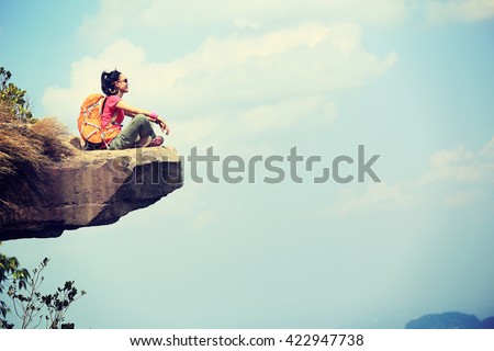 successful young woman backpacker sit on seaside mountain top cliff edge