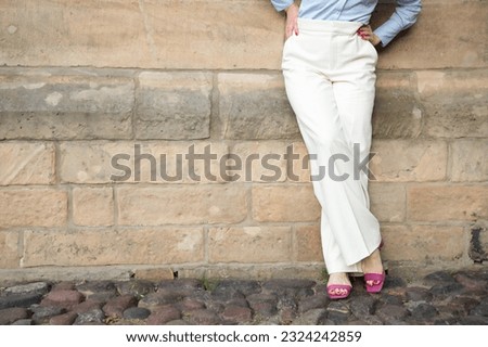 a successful young woman in white trousers and a blue shirt. the woman is leaning against the wall. A shortened shot of a woman's legs in classic trousers. copy space