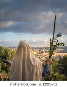 Succot (Feast of Tabernacles) in Jerusalem: Jewish man in a Tallit praying while waving the Four Species, with a view towards the Temple Mount, the Old City and the Mount of Olives