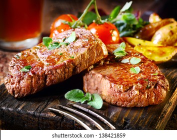 Sukkulente, saftige Portionen von gegrilltem Filet Steak, serviert mit Tomaten und Bratgemüse auf einem alten Holzbrett