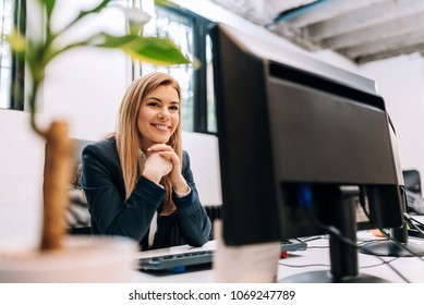 Erfolgreiche lächelnde Geschäftsfrau, die vor einem Computer im Büro sitzt.