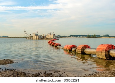 Suction Dredger In A Dutch River Sucks Sand And Gravel From The River Bottom And Transports It Via A Floating Pipeline With Orange Floats To The Shore.