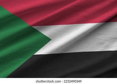 Sudan flag with big folds waving close up under the studio light indoors. The official symbols and colors in fabric banner