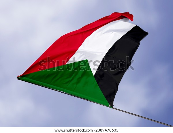 Sudan\'s flag is\
isolated on a sky background. flag symbols of Sudan. close up of a\
Sudanese flag waving in the\
wind.